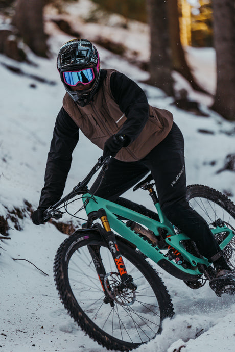 Mountainbiker im Schnee mit brauner Weste und grünem Fahrrad