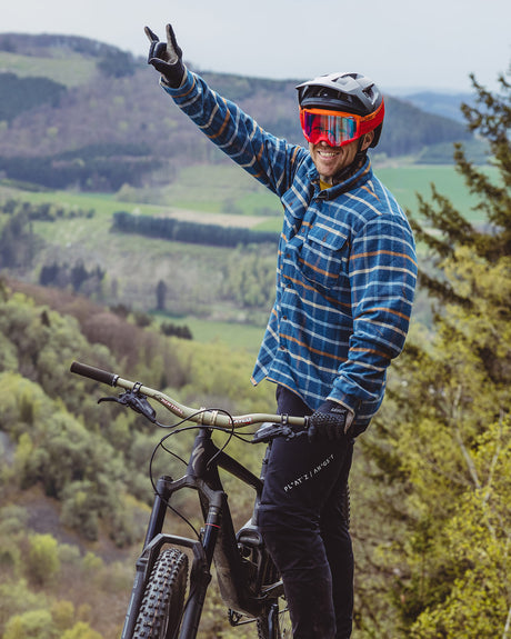 Mountainbiker in blauen kariertem Hemd zeigt Hörner mit der Hand