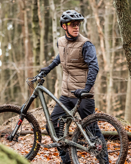 Mountainbiker mit brauner Weste steht vor Mountainbike